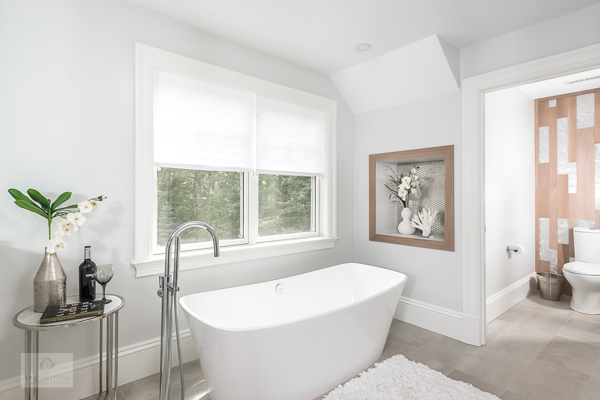 bath design with freestanding tub, wall feature, recessed storage, and glass and metal table
